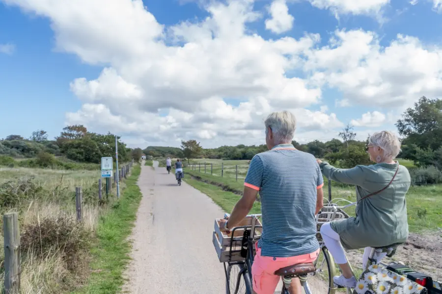 Echtpaar fietst door de duinen en wijst naar knooppunten renesse